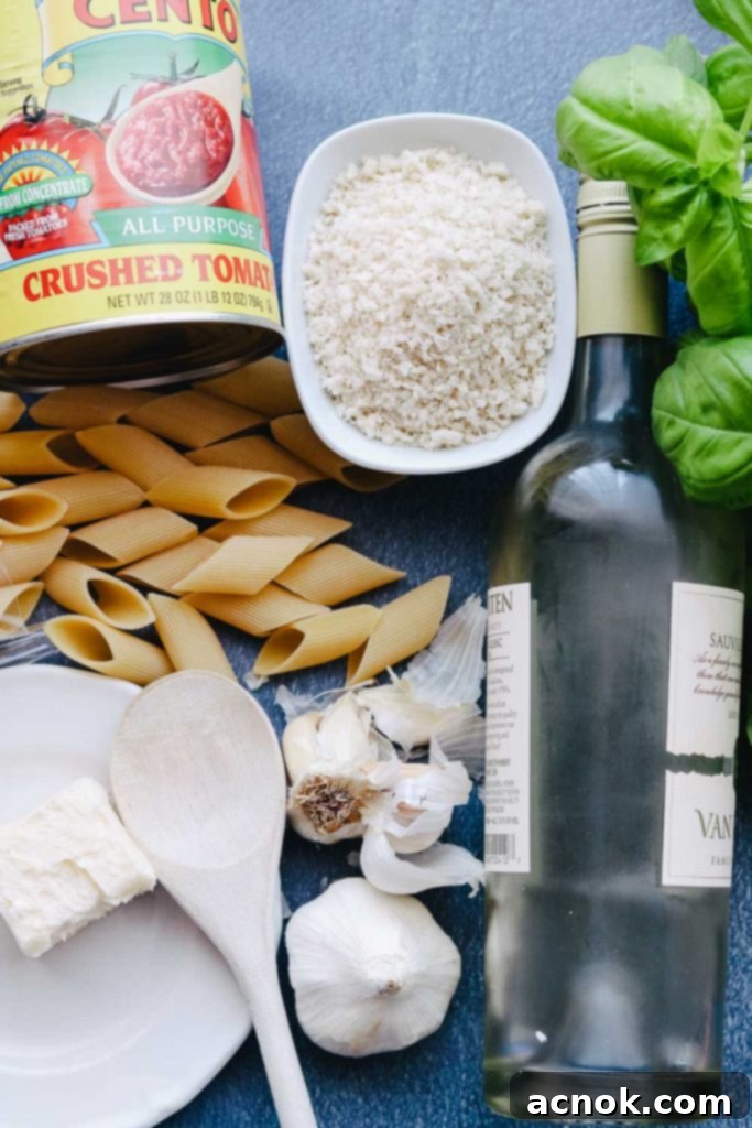 Ingredients for Tomato Butter Sauce Pasta: canned tomatoes, pasta, white wine, garlic, breadcrumbs, and fresh basil laid out on a table.