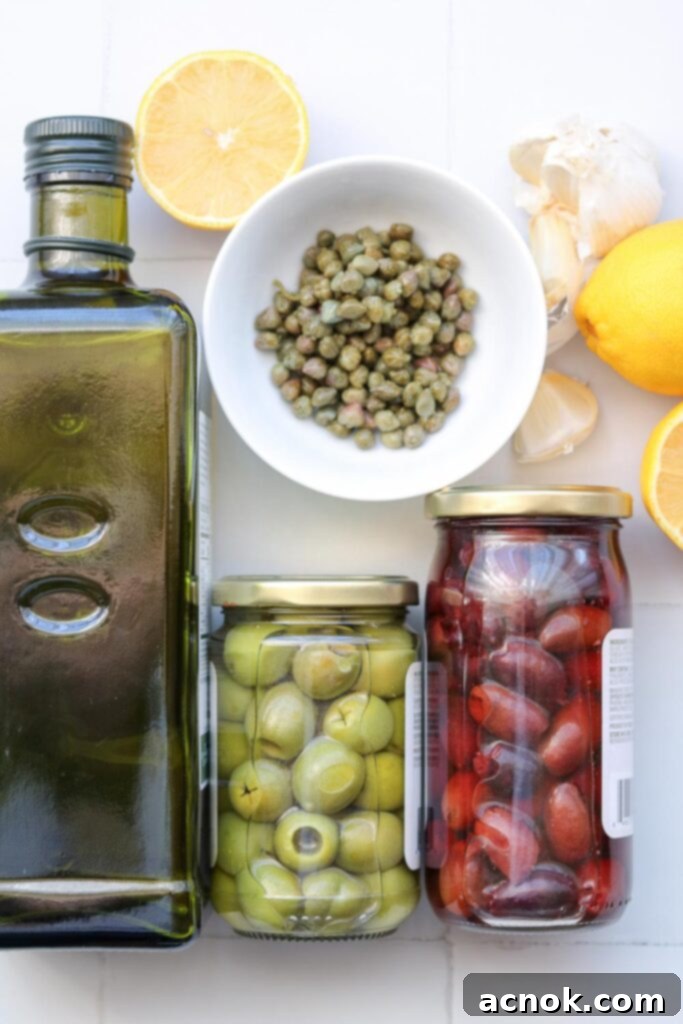 Fresh ingredients for mixed olive tapenade: olive oil, pitted Kalamata & Castelvetrano olives, capers, lemon and garlic arranged on a wooden board.
