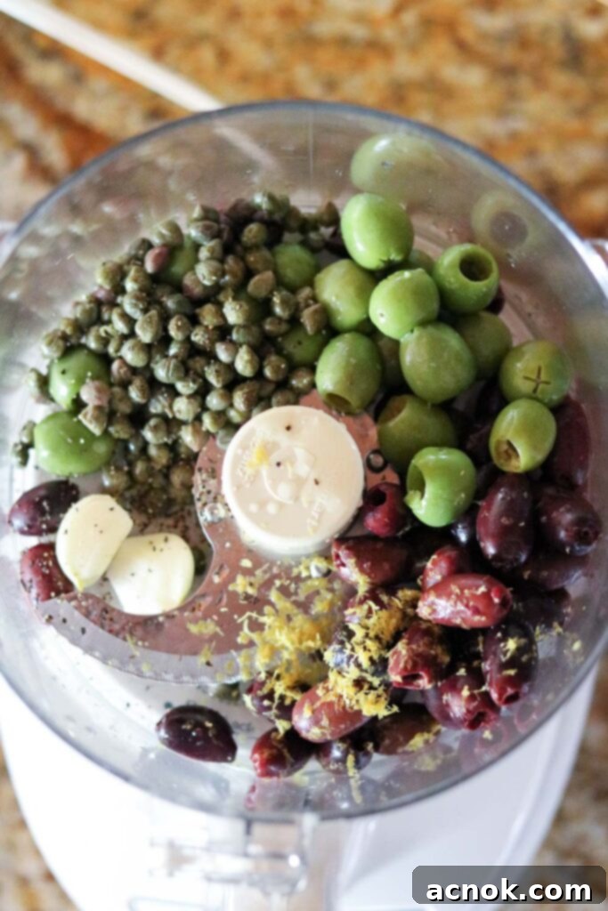 Pitted Kalamata and Castelvetrano olives, capers, lemon zest, garlic, and a splash of lemon juice are added to a food processor bowl.