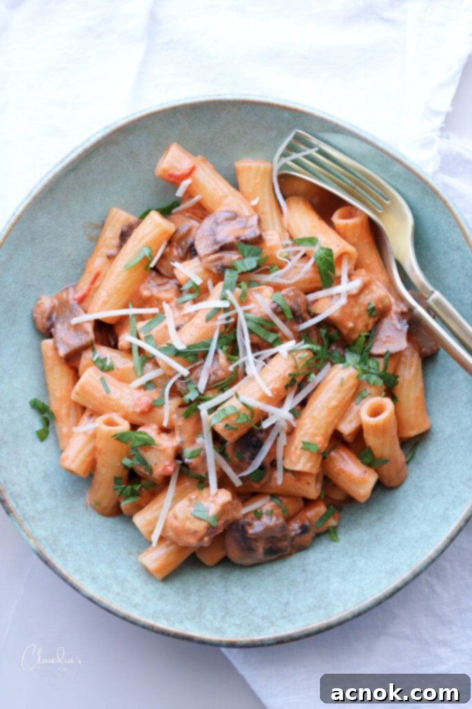 A vibrant blue bowl filled with Creamy Tomato Chicken and Mushroom Pasta, garnished with fresh herbs and golden silverware.
