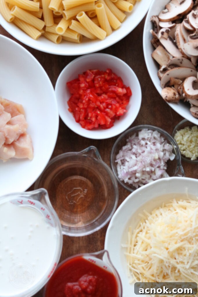 A selection of fresh ingredients including olive oil, chopped chicken, sliced mushrooms, shallots, garlic, and fresh Roma tomatoes, laid out for creamy tomato chicken and mushroom pasta preparation.