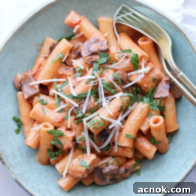 A beautifully plated serving of creamy tomato chicken and mushroom pasta in a blue bowl.