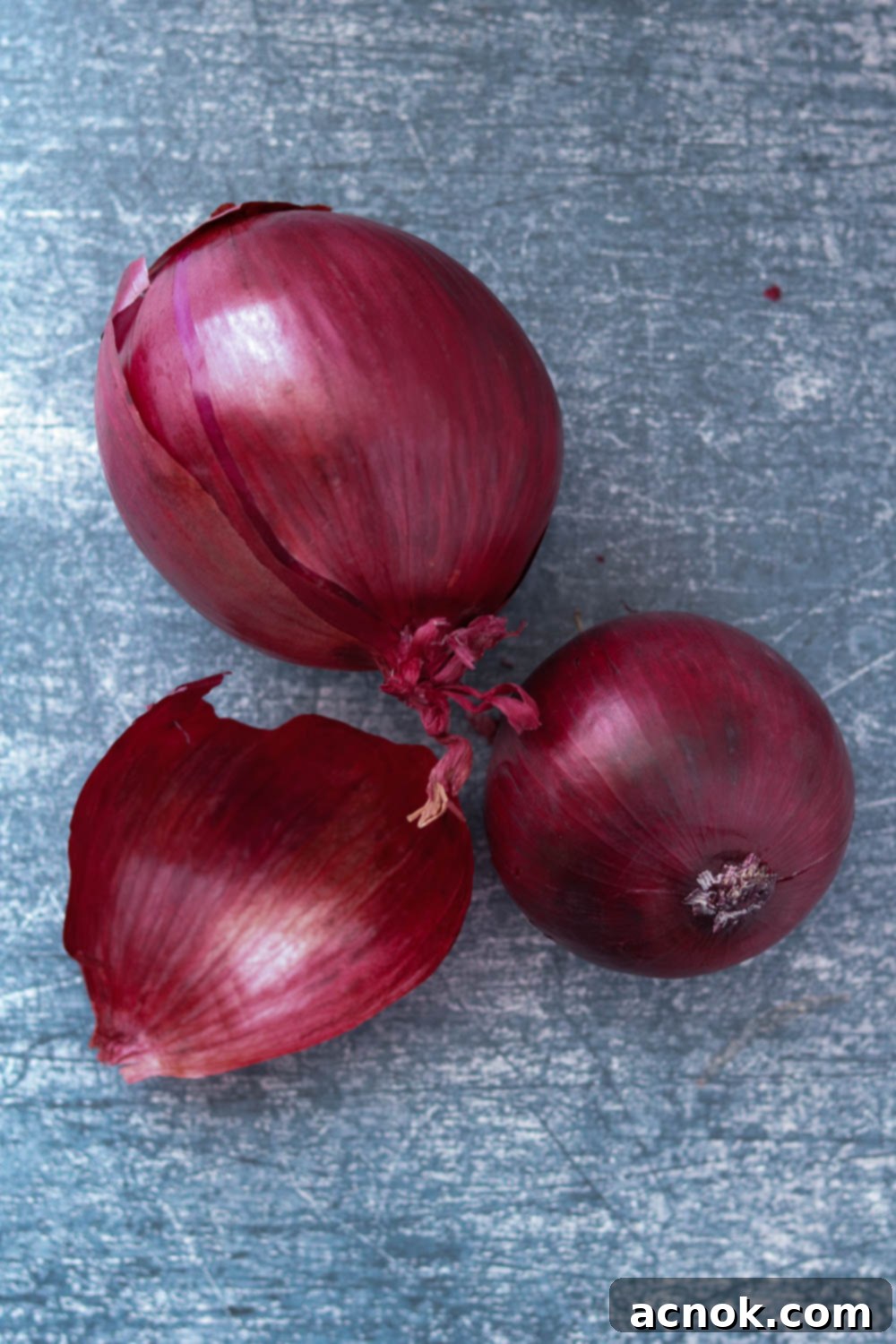Whole, unpeeled red onions on a cutting board, ready for slicing.