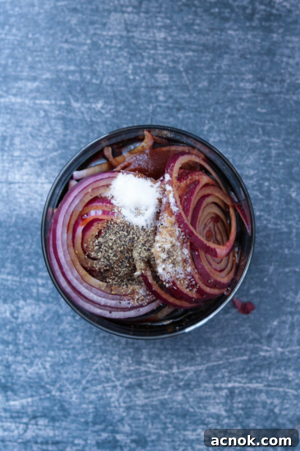 Thinly sliced red onions in a bowl with balsamic vinegar, olive oil, and seasonings.