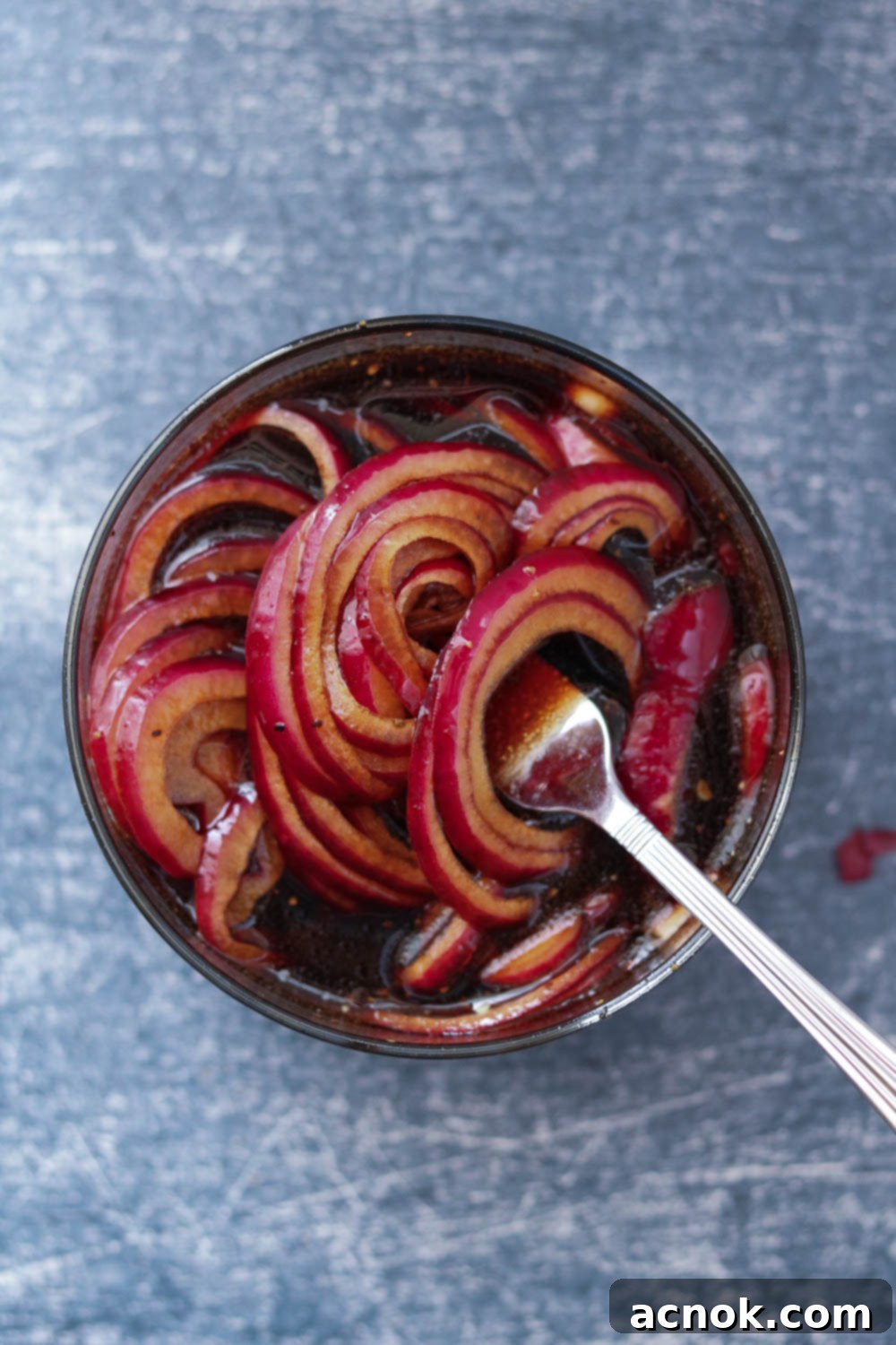 Jar of red onions marinating in balsamic vinegar on a countertop.
