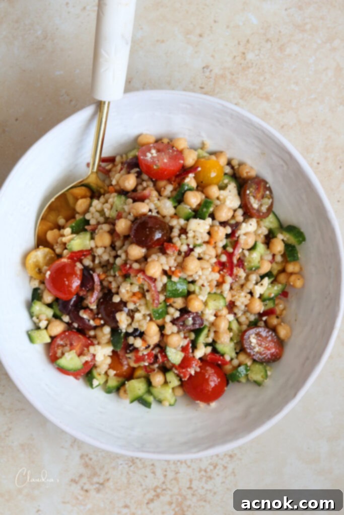 Top view of Pearl couscous salad with feta and chickpeas in a white bowl, freshly tossed