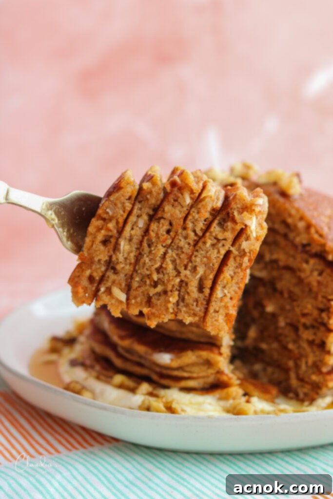 Close-up of a wedge of coconut carrot cake pancake with creamy sauce on a fork
