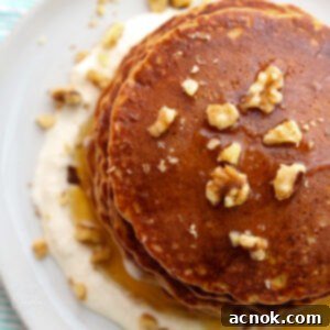 Overhead shot of coconut carrot cake pancakes with cream cheese glaze, butter, and toasted walnuts on a white plate