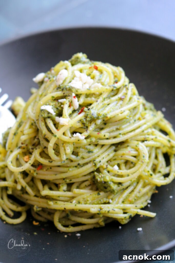 Vibrant green kale pistachio feta pesto on spaghetti in a stylish black bowl, garnished with fresh feta and red pepper flakes.