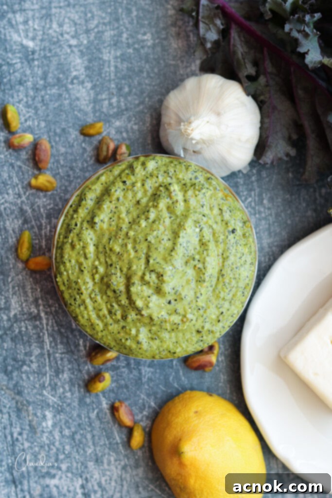 A bowl of freshly made kale pistachio and feta pesto, surrounded by the ingredients like kale, pistachios, feta, and olive oil, ready to be used with pasta or other dishes.