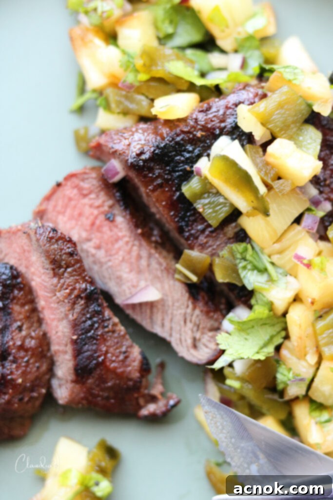 Juicy, perfectly cooked hangar steak seasoned with an Ancho Chile rub, topped with a generous serving of fresh grilled pineapple jalapeno salsa, presented on a plate.