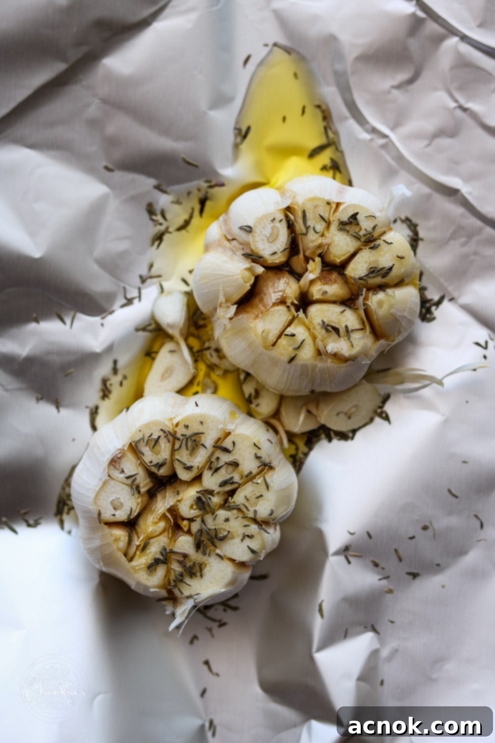 fresh garlic with tops removed and drizzled with olive oil, thyme and salt, ready for roasting