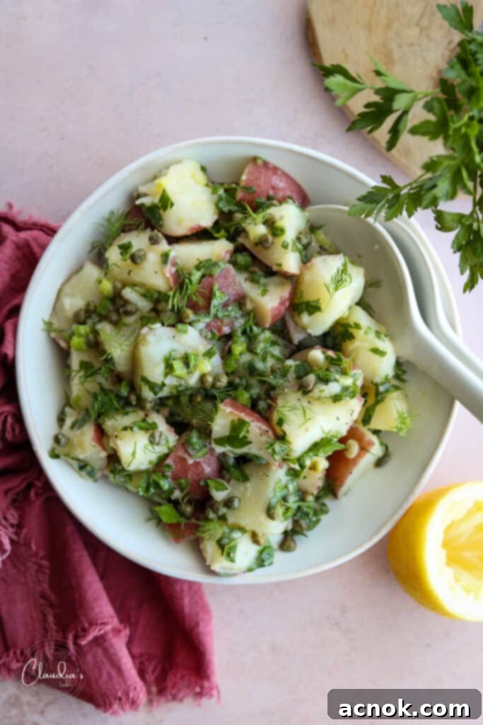 Lemon caper potato salad in white bowl with red napkin, garnished with fresh herbs and lemon slices