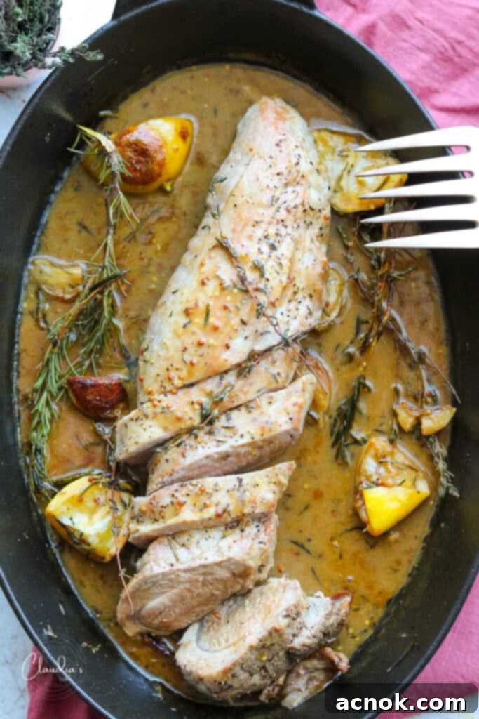 Cooked sliced pork tenderloin with lemon herb pan sauce in a black pan with fresh aromatics