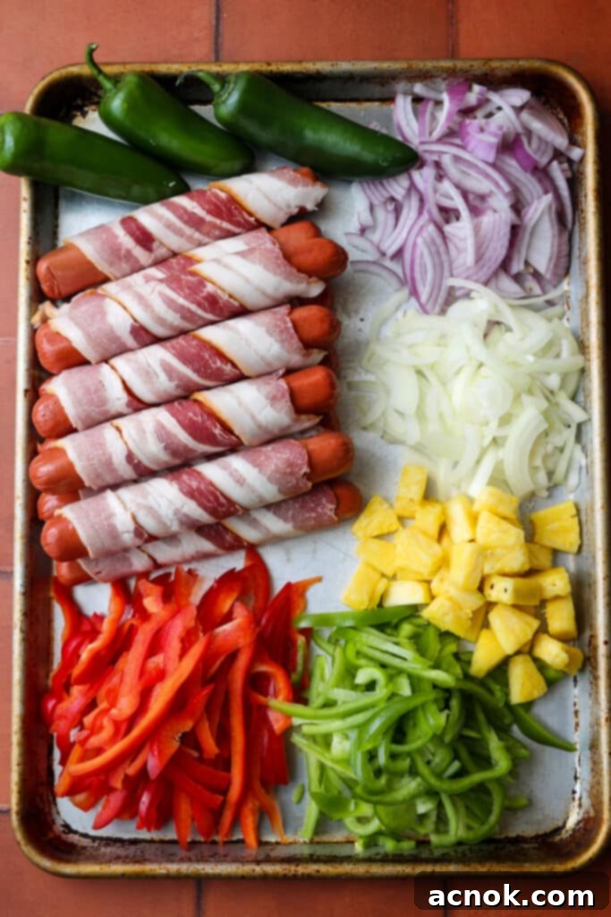 Ingredients for LA style street hot dogs laid out on a sheet pan, including bacon-wrapped hot dogs, peppers, and onions.