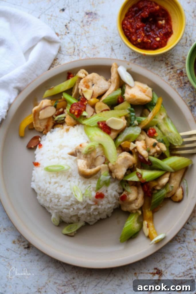 Easy almond chicken stir-fry served with steamed rice and a side of Asian chili garlic sauce for added flavor.