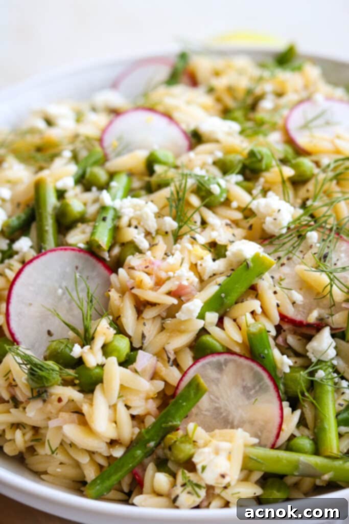orzo salad with asparagus and peas in white bowl with lemons in the background
