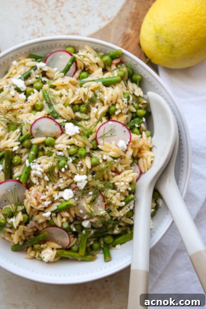 orzo salad with asparagus and peas in white bowl with serving utensils and lemon 