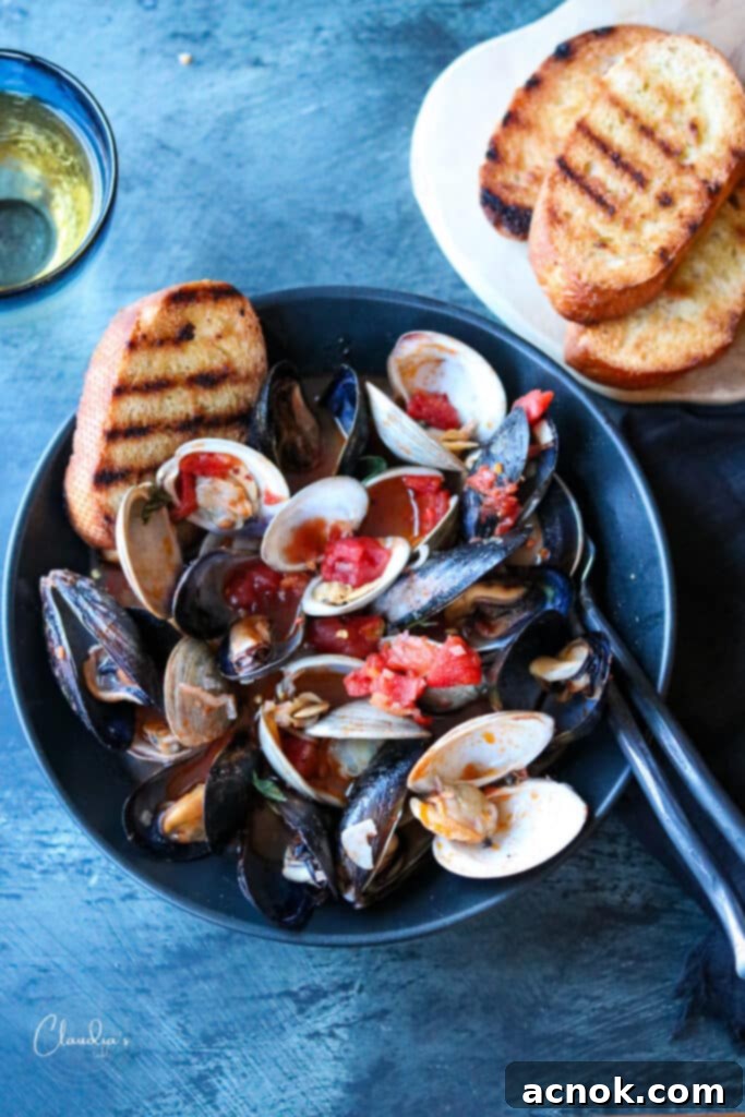 Mussels and clams served in a black bowl with toasted bread on the side, showcasing the rich tomato broth.