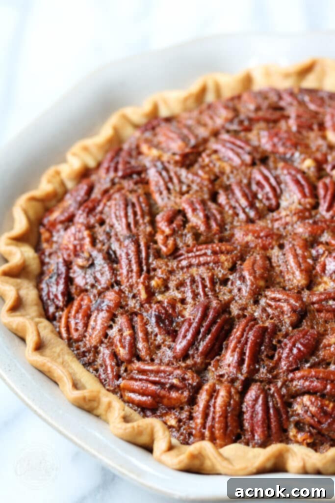 Close-up view of a perfectly baked Brown Butter Bourbon Pecan Pie in a white pie dish, showcasing its golden crust and rich pecan filling.