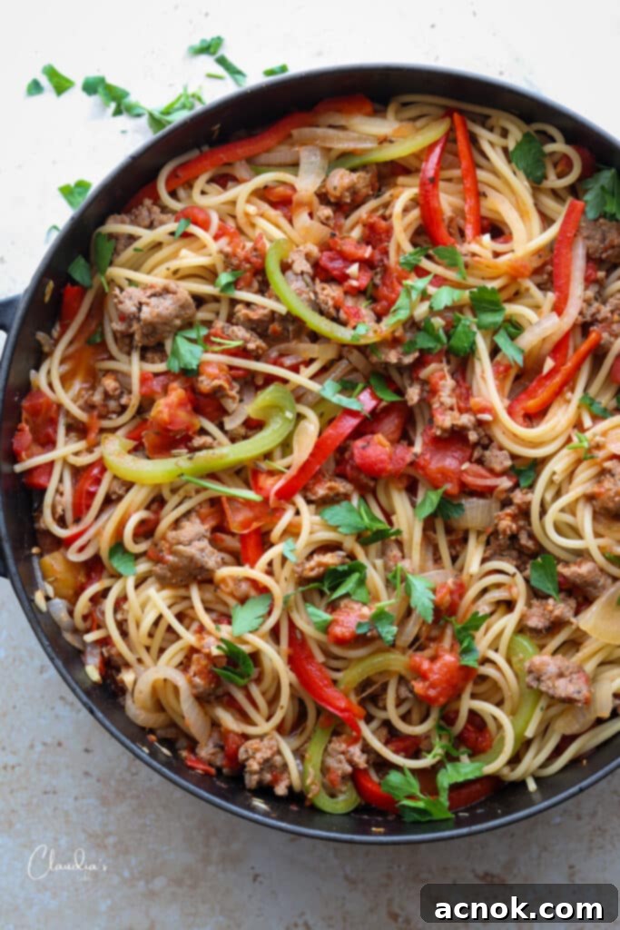 Delicious spicy Italian sausage and pepper spaghetti served in a black pan, garnished with fresh herbs.