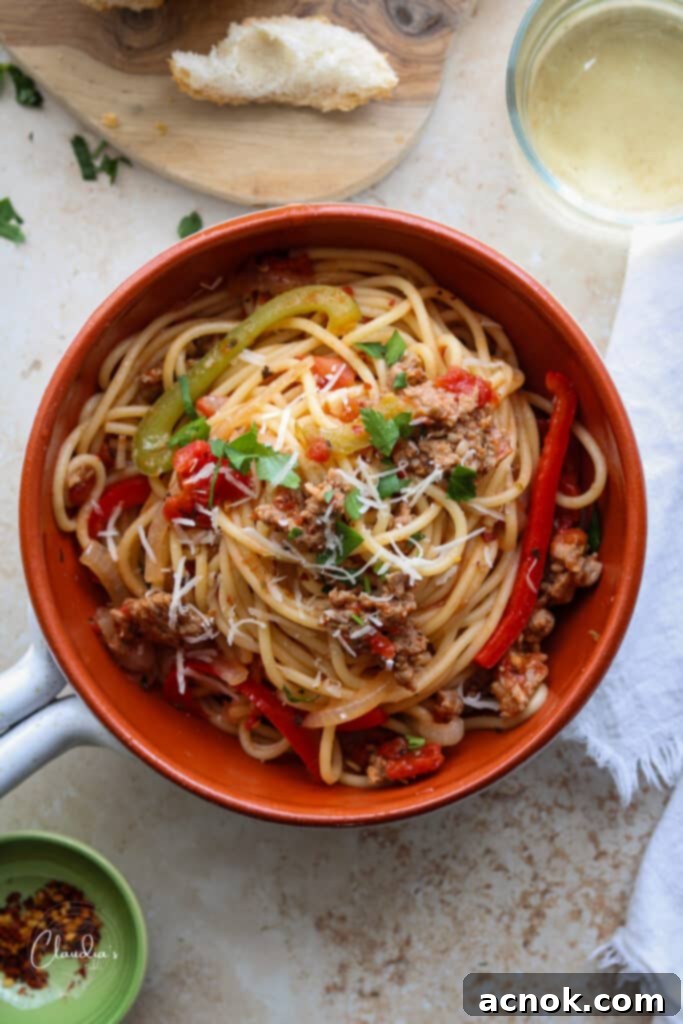 Top view of a beautifully plated spicy Italian sausage and pepper spaghetti, accompanied by crusty bread and a glass of white wine.