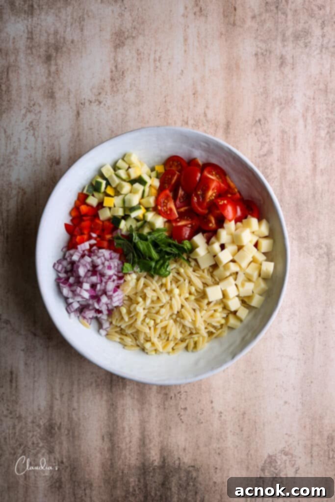 Assembling the Summer Pesto Orzo Pasta Salad in a white bowl.