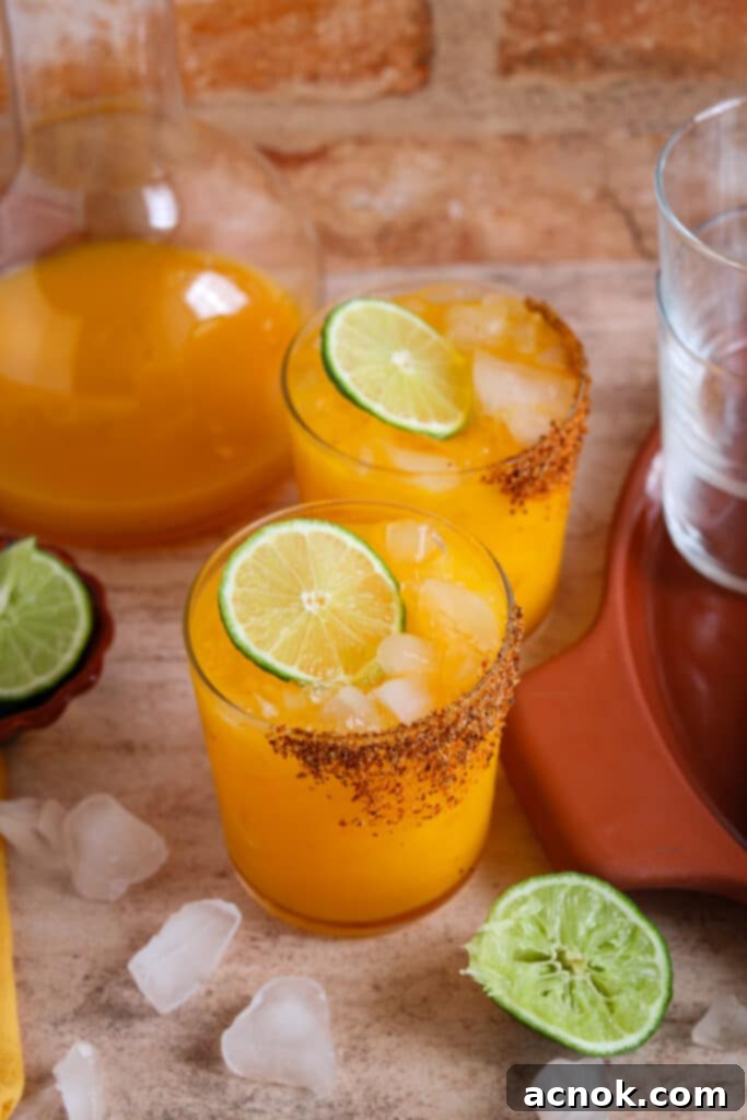 two tangerine margaritas garnished with lime wheels and a Tajin rim
