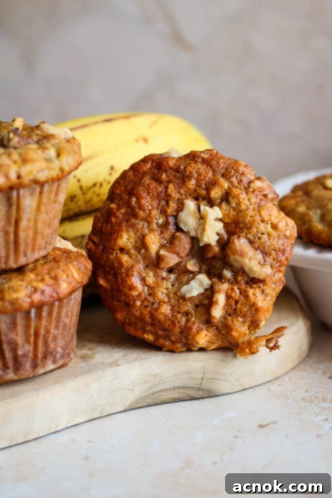 Golden brown banana and oat muffin with walnuts on a rustic wood board, showcasing its fluffy texture.