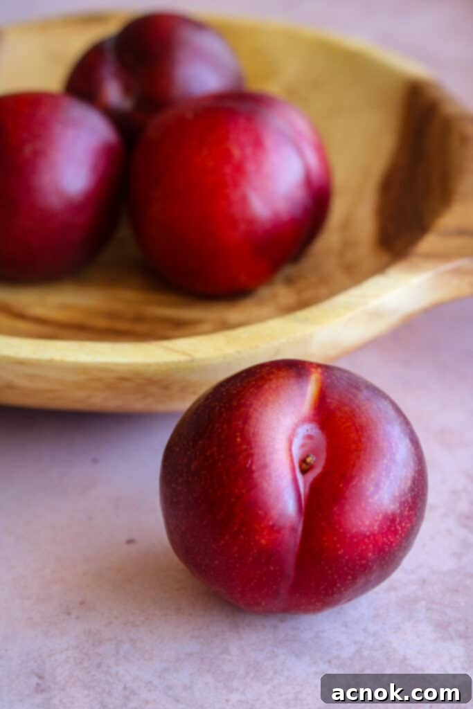 Fresh red plums in a rustic wooden bowl, ready for slicing.