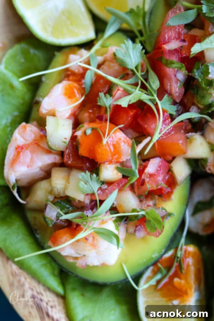 Shrimp avocado salad in avocado boat garnished with micro cilantro and lime wedges, showcasing a healthy and delicious meal.